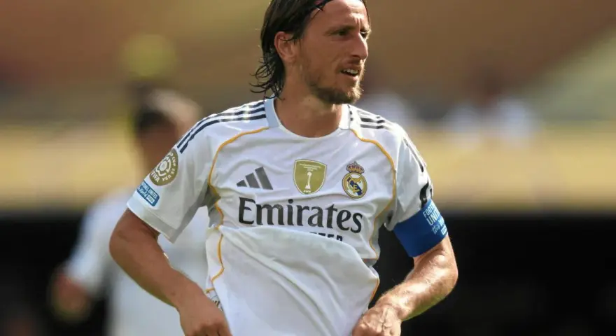 Luka Modrić w białej koszulce Realu Madryt, gdzie gra, z opaską na ramieniu.