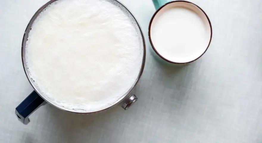Un pot de lait chaud avec une fine peau de lait à la surface, à côté d'une tasse remplie de lait frais.