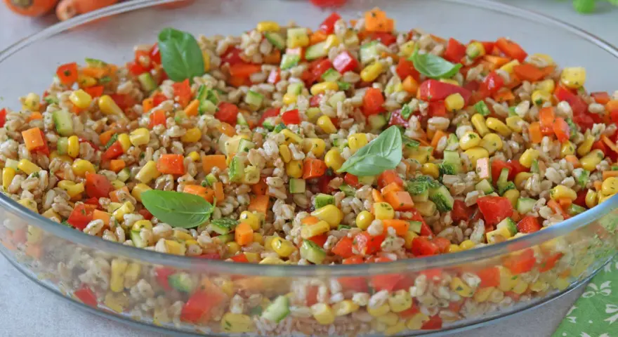 Insalata di farro colorata con mais, peperoni, zucchine e carote, guarnita con foglie di basilico fresco. Un piatto estivo e salutare.