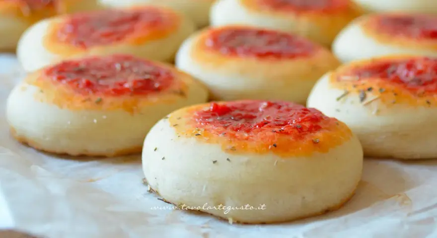 Pizzette fatte in casa, piccole e invitanti, con un soffice impasto e un tocco di pomodoro e erbe aromatiche.