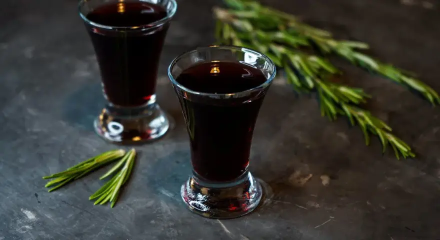 Dwa kieliszki ciemnego, aromatycznego nalewki z czernic, ozdobione gałązkami rozmarynu.