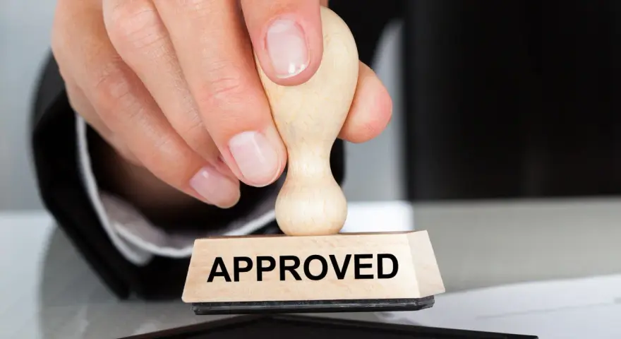 Dłoń z pieczątką "APPROVED" nad poduszką z tuszem. To symbol zatwierdzenia, jak certyfikat AEO.