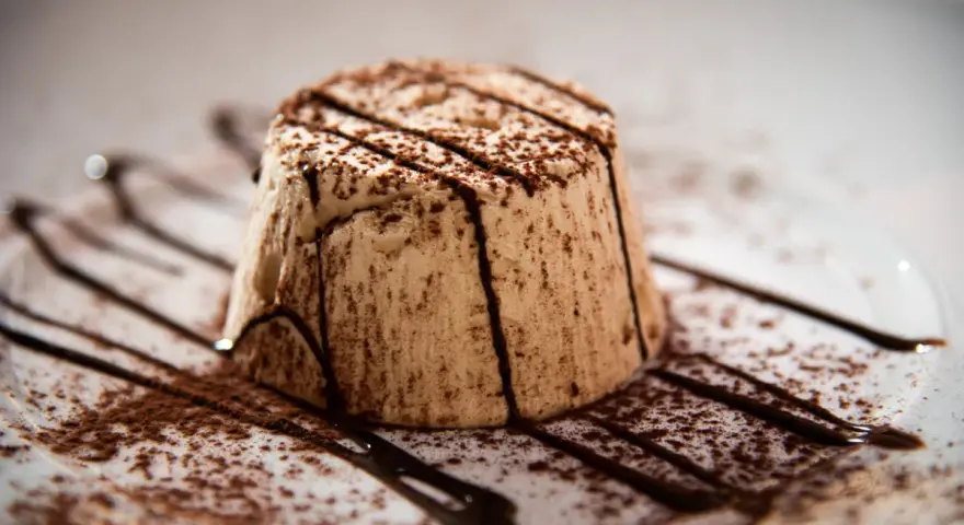Delizioso parfait di mandorle, spolverato di cacao e decorato con scaglie di cioccolato fondente su un piatto bianco.