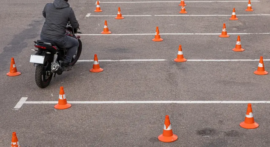 Motocyklista w kasku pokonuje tor przeszkód z pachołków, ćwicząc jazdę na prawo jazdy **kategoria a2**.