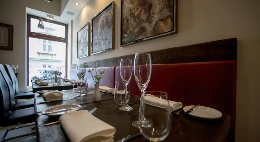 Elegancko nakryte stoły w restauracji z gwiazdką Michelin w Polsce. Czerwone obicia, obrazy na ścianach i kieliszki zapraszają na wyjątkowe doznania kulinarne.