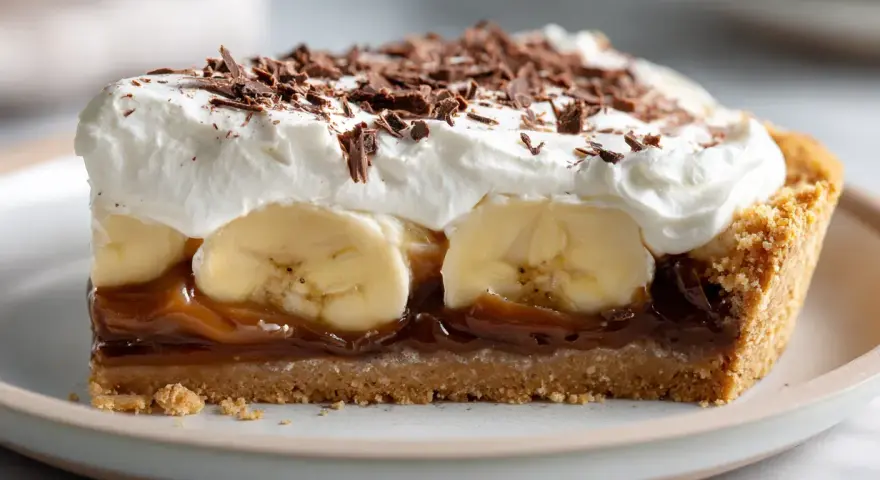En bit krämig banoffee paj med banan, kolasås, vispgrädde och chokladströssel.