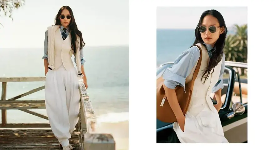 Donna con stile smart casual, indossa gilet, camicia azzurra, pantaloni bianchi ampi e cravatta, con sfondo marino.
