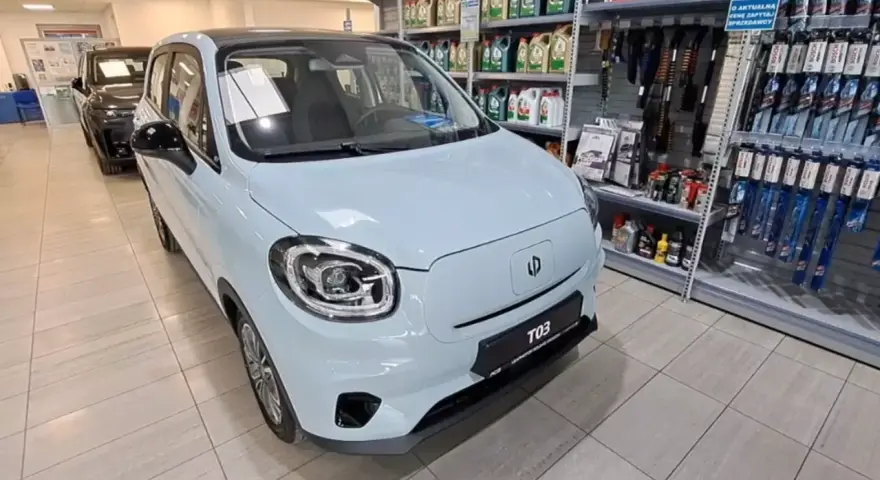 Jasnoniebieski Leapmotor T03 stoi w salonie samochodowym obok półek z akcesoriami.