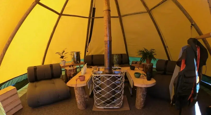 Mysig interiör i ett tipi-tält på Sorsele camping. Här finns sittplatser, ett bord och en kamin för värme.