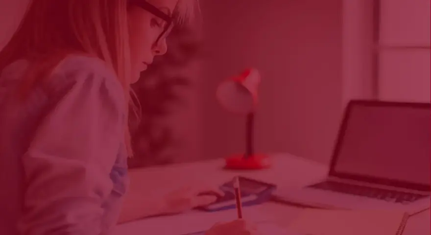 Kobieta z zeszytem i kalkulatorem zastanawia się, ile kosztują studia zaoczne. Obok leży laptop.