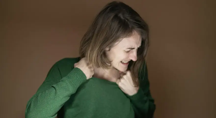 Kobieta w zielonym swetrze zaciska zęby, szarpie się za ubranie. Widać wyraźny stres przed seksem, niepokój maluje się na jej twarzy.