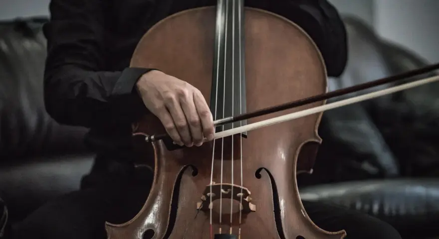 Eine Hand hält den Bogen über dem Violoncello-Instrument, bereit, die Saiten zum Klingen zu bringen.