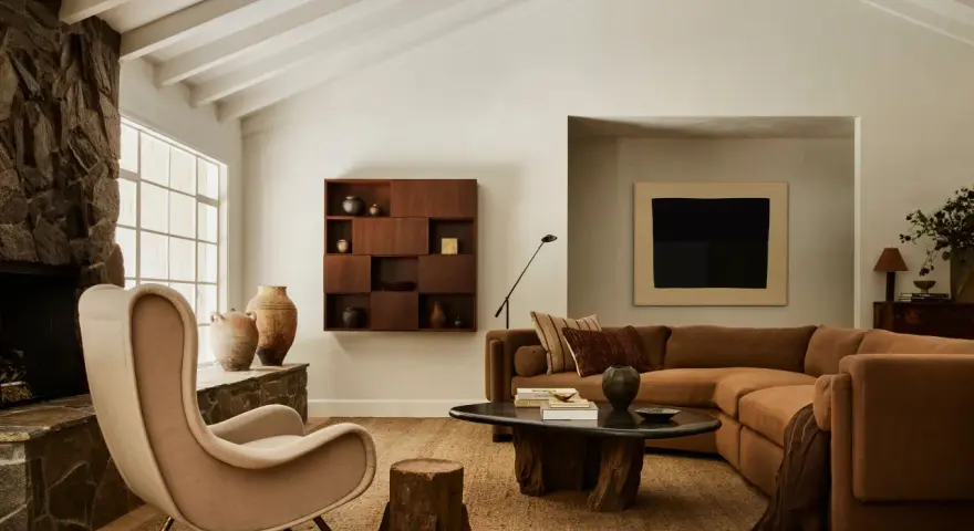 Un acogedor salón con chimenea de piedra, sillón de tela, sofá marrón y mesa de centro de madera. El arte de pared y las cerámicas añaden un toque de estilo chino hogar.