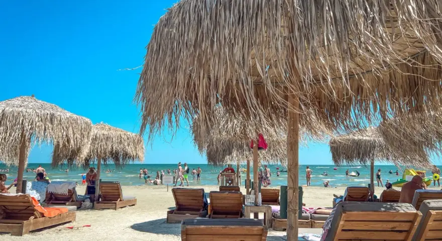 Słoneczny dzień na plaży w Rumunii nad Morzem Czarnym. Leżaki i parasole z trawy zapraszają do odpoczynku.