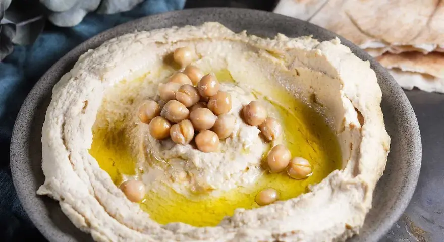 Krämig hummus med kikärtor och olivolja, perfekt för ett enkelt hummus recept. Serveras med pitabröd.