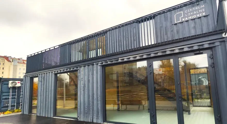 Nowoczesne centrum lokalne Kamionek, zbudowane z kontenerów. Ten innowacyjny kamionkowy materiał budowlany tworzy przestrzeń z przeszklonymi fasadami i balkonem.
