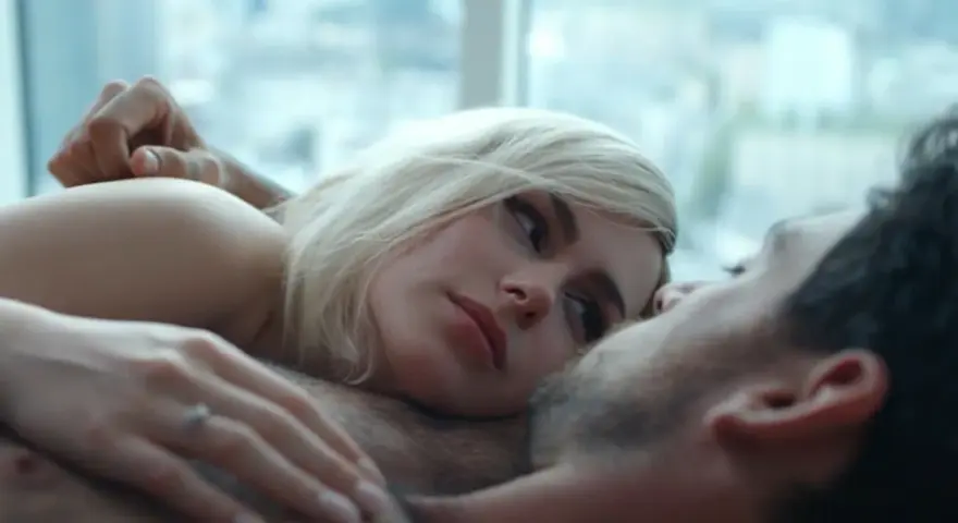 Blondynka i brunet leżą blisko siebie, ich ciała stykają się. Intymna scena, która sugeruje seks na scenie.
