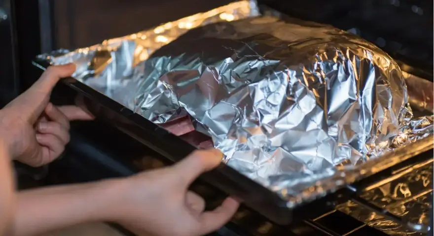 Mains dans un plat recouvert d'aluminium au four, prêt à cuire.