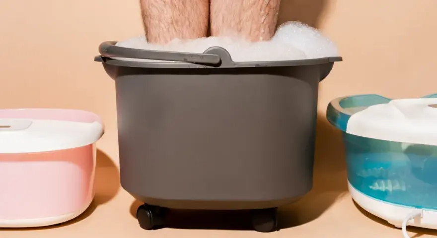 A person's legs are submerged in a foamy foot bath, part of a home foot detox setup with other foot spa machines.