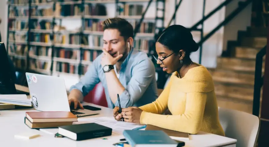 Studenti universitari collaborano a un progetto, immersi in libri e tecnologia.