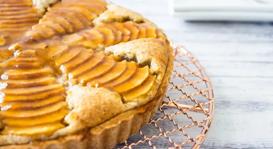 Deliciosa tarta de pera francesa, con peras laminadas y glaseado dorado, enfriándose sobre una rejilla de cobre.