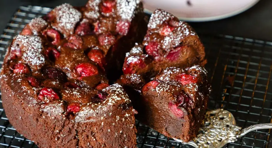 Ein saftiger schoko kirsch kuchen, bestäubt mit Puderzucker, wird auf einem Gitter präsentiert. Eine Gabel hebt ein Stück ab.