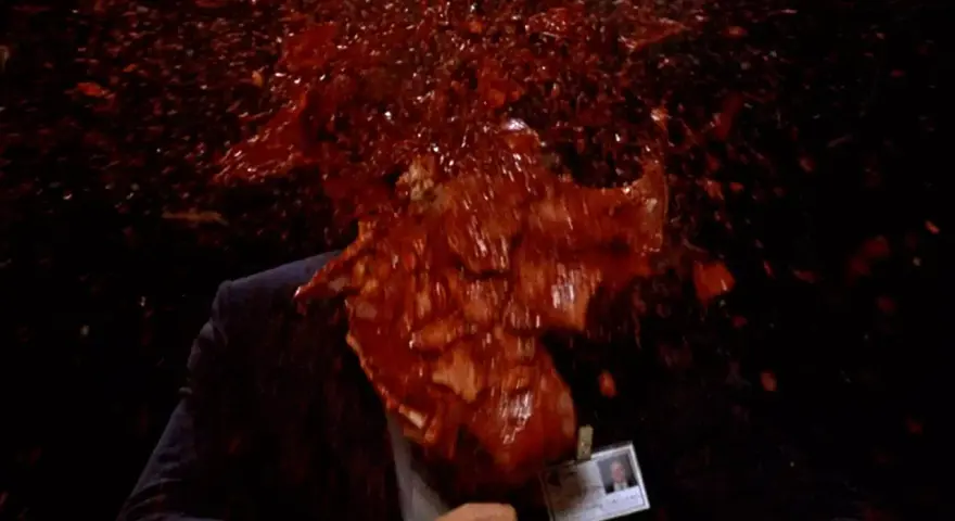 Un uomo in giacca e cravatta, vittima di un evento cruento, con sangue e detriti che esplodono in un'immagine tipica di un genere cinematografico con scene truculente.
