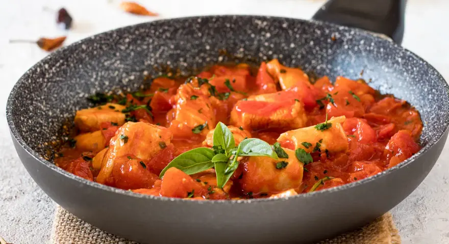 Bocconcini di pollo in padella con pomodoro e basilico, un piatto succulento pronto per essere gustato.