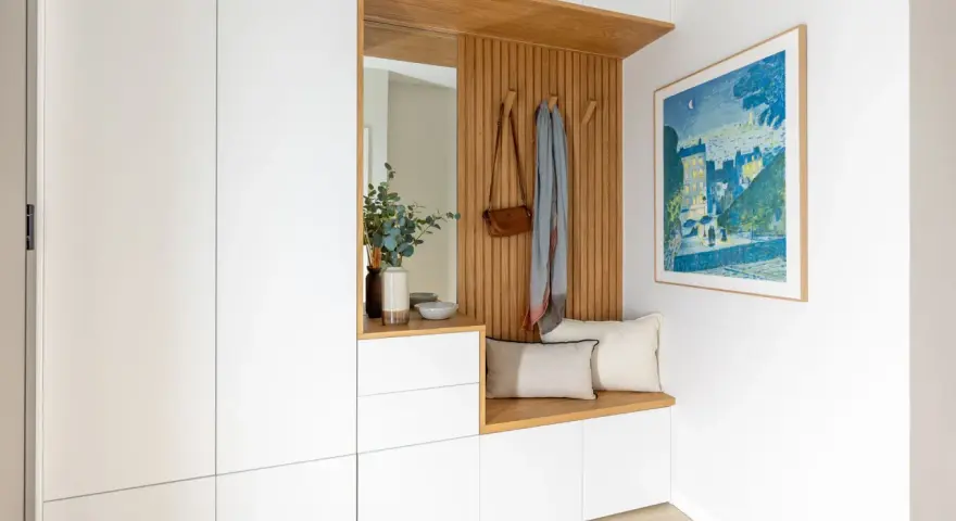 Ideas para decorar recibidor pequeño: banco de madera, espejo, perchero con bolso y bufanda, cuadro y armarios blancos.