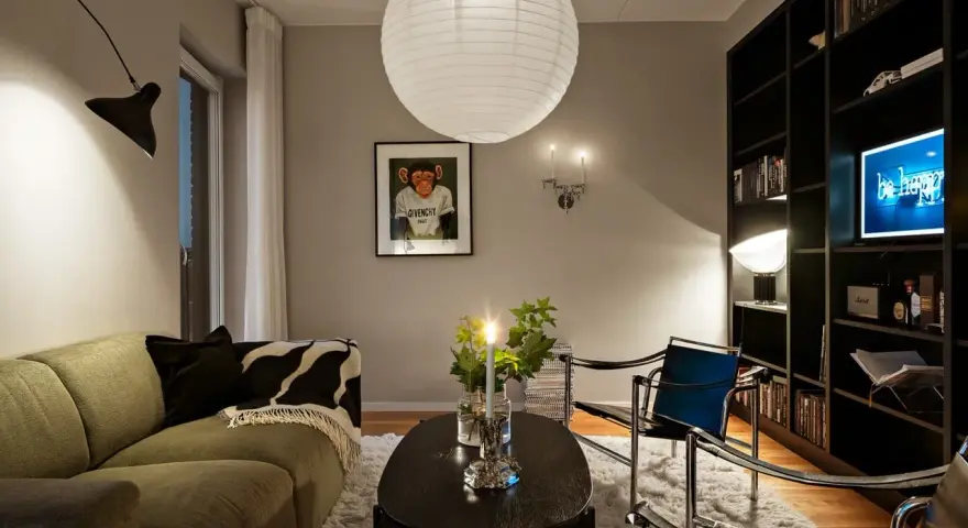 Mysig vardagsrumsmiljö med en stor taklampa, en svart vägglampa och en bokhylla full med böcker. Perfekt lampor inspiration för ditt hem.