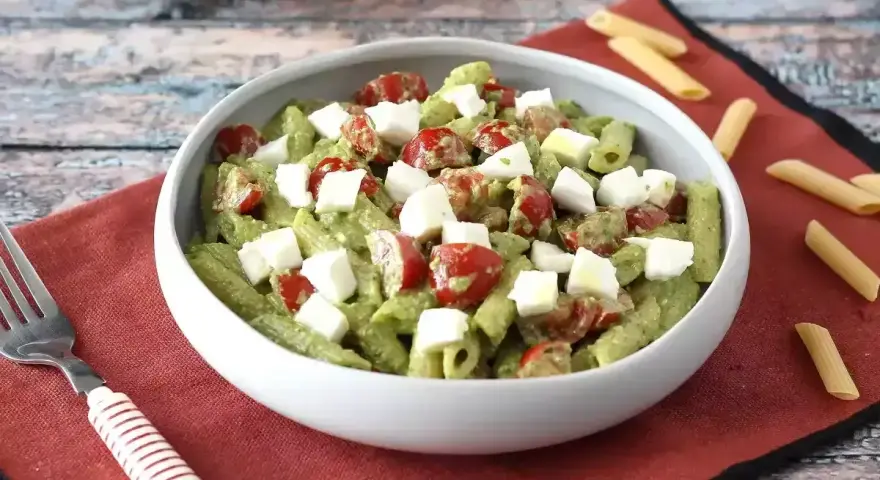 Makaron z pesto ze słoika przepis: penne z zielonym pesto, pomidorkami koktajlowymi i kostkami mozzarelli w białej misce.