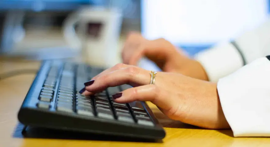 Händer med mörkt nagellack och ringar skriver på ett tangentbord, kanske ett brev på engelska.