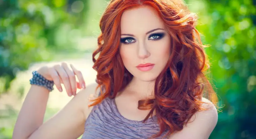 Une femme aux cheveux roux et au maquillage smoky eyes parfait, idéal pour un tuto smoky eyes débutant.