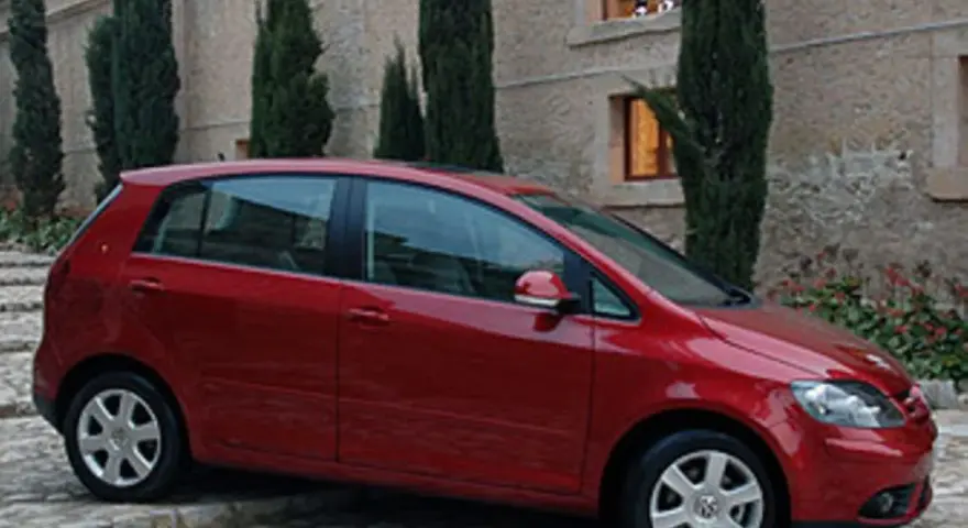 Roter VW Golf Plus mit Automatikgetriebe, der vor einem Steingebäude parkt. Mögliche Probleme mit dem Automatikgetriebe sind ein Thema.