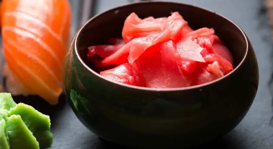 Miseczka z różowym imbirem do sushi, obok kawałek łososia i zielone wasabi.