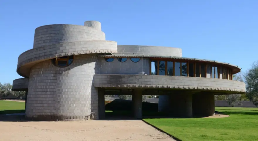 Bâtiment circulaire en béton, exemple des structures conçues par Frank Lloyd Wright, avec des fenêtres rondes et une façade en gradins.