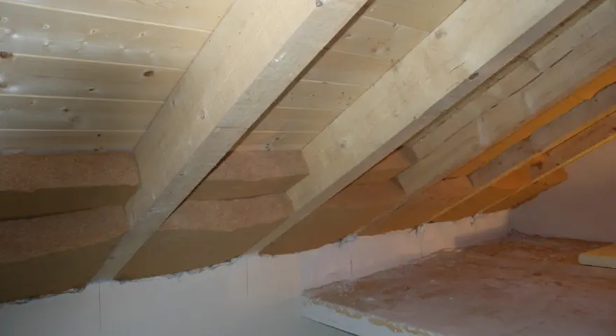 Isolamento tetto dall'interno fai da te: pannelli isolanti in fibra di legno tra le travi di legno grezzo, con sottotetto in perline.