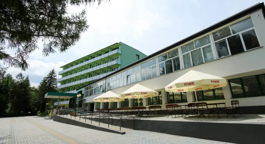 Tanie sanatorium prywatnie: zielony budynek z balkonami i tarasem z parasolami Tyskie.