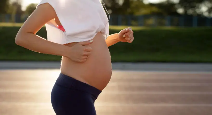 En gravid kvinna springer på en löparbana i solnedgången.