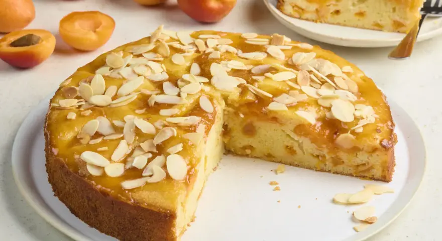 Saftiger aprikosenkuchen mit frischen aprikosen und Mandelblättchen, ein Stück bereits angeschnitten.