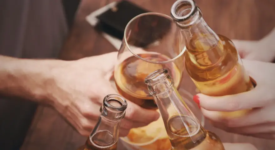 Ludzie wznoszą toast butelkami piwa i kieliszkiem alkoholu.