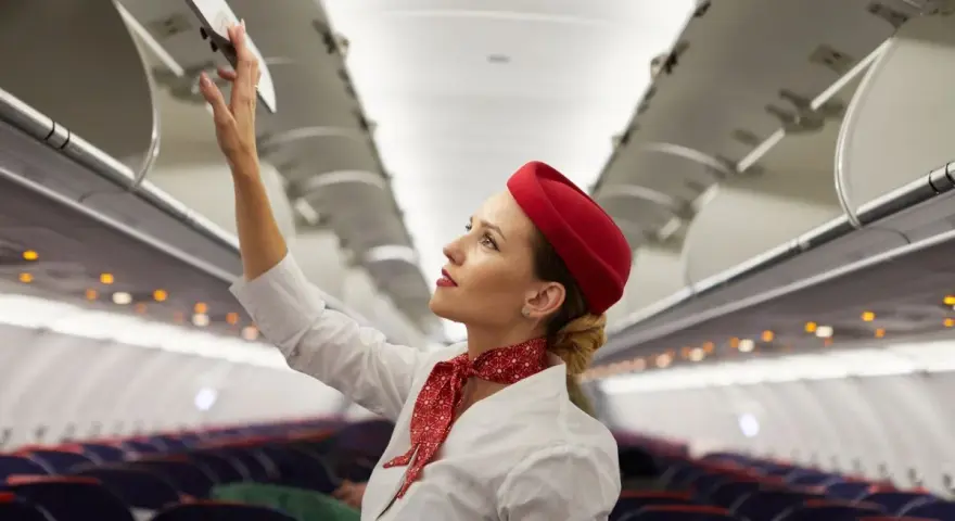 Flugbegleiterin schließt Gepäckfach. Ein Beruf, der mehr als nur das Flugbegleiter Gehalt bietet.