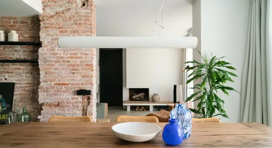 Salón con pared de ladrillo visto, mesa de madera con jarrones y planta.