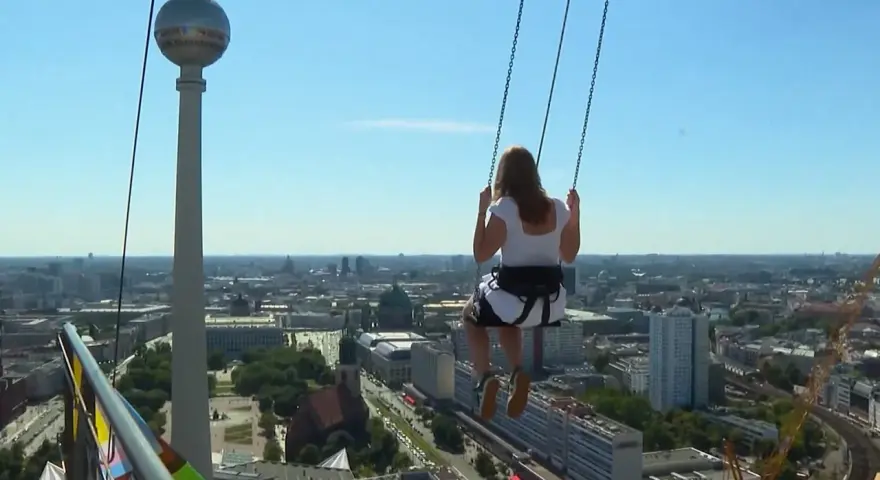 Frau schaukelt hoch über Alexanderplatz Berlin, mit Blick auf die Stadt und den Fernsehturm.