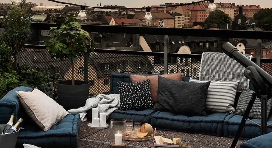 Gemütliche Lounge-Ecke auf einem grossen Balkon mit Blick über die Stadt. Kissen, Decken, Kerzen und ein Teleskop laden zum Entspannen ein.