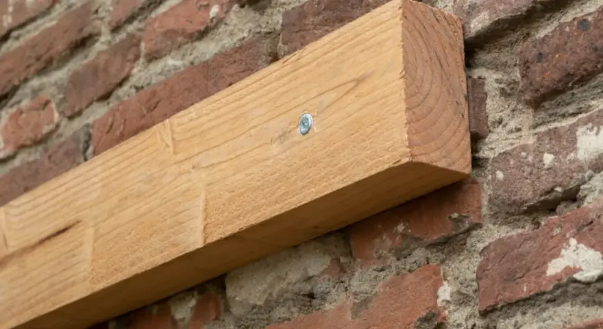 Ein Holzbalken wird mit einer Schraube an einer Ziegelwand befestigt.