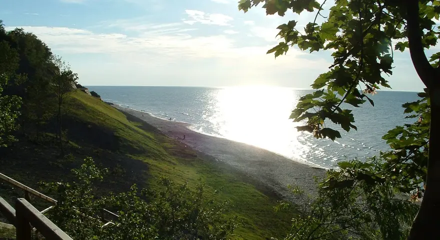 Słoneczny dzień nad morzem, łagodne zbocze porośnięte trawą schodzi do plaży. Jastrzębia Góra atrakcje to spacer po klifie i podziwianie widoków.
