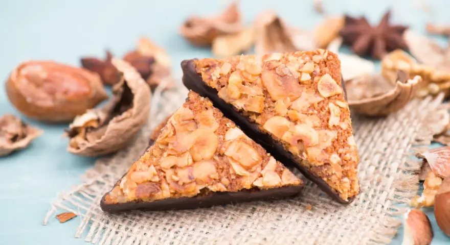 Zwei dreieckige Nussecken mit Schokoladenboden, bestreut mit gehackten Nüssen. Ein köstliches nussecken rezept zum Nachbacken.