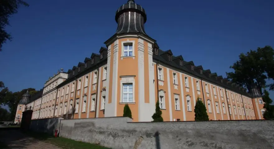 Klasztor Paradyż, okazały budynek z pomarańczowo-białą fasadą i wieżyczką, otoczony murem.