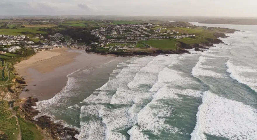 Aerial videography captures a coastal village with a sandy beach and rolling waves.
